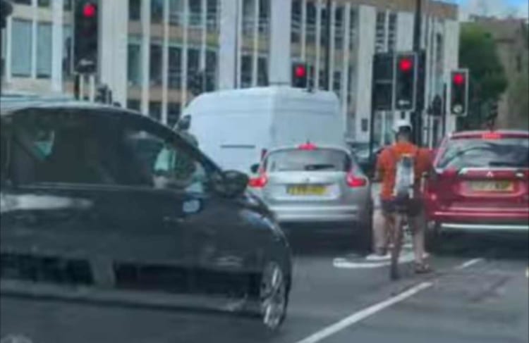 前を行く自転車に乗るライダーに背負われているイヌ。よく見るとその姿がワイルド&クールだった！！