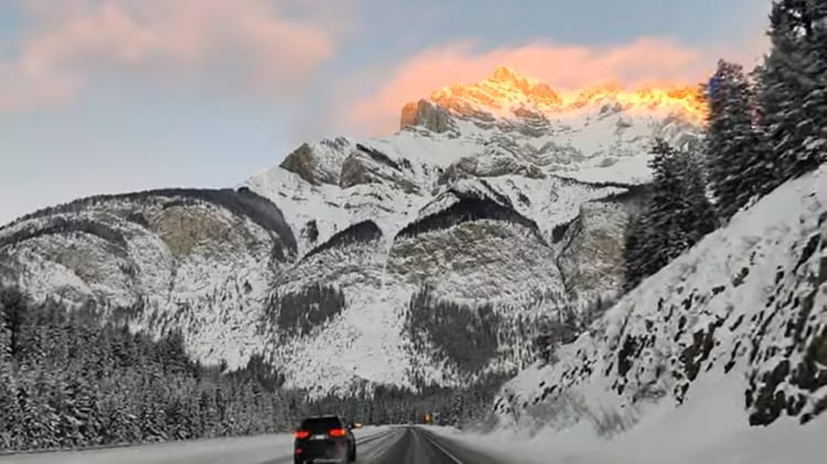 雪山を眺望する道路を運転中に見た日の出、その様子が美しすぎる。山にかかる黄金の光が神々しい