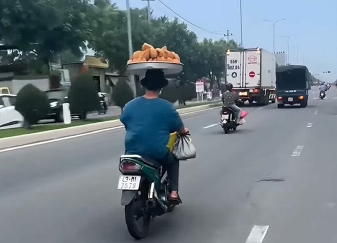 バランス感覚がスゴすぎる！山盛りのドーナツのトレーを頭に乗せて男性がバイクで走っていく！！【海外・動画】
